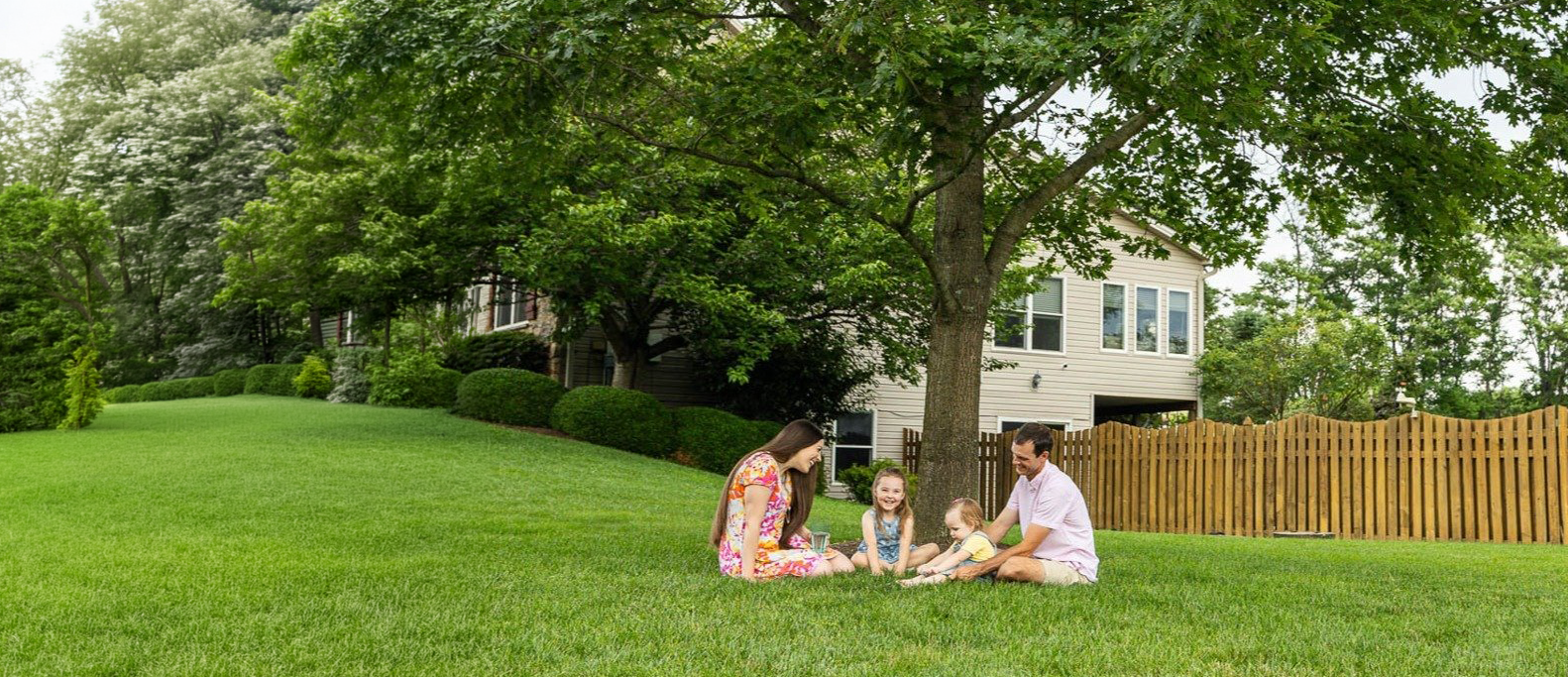 A family relaxing on a beautifully maintained lawn under a mature shade tree.